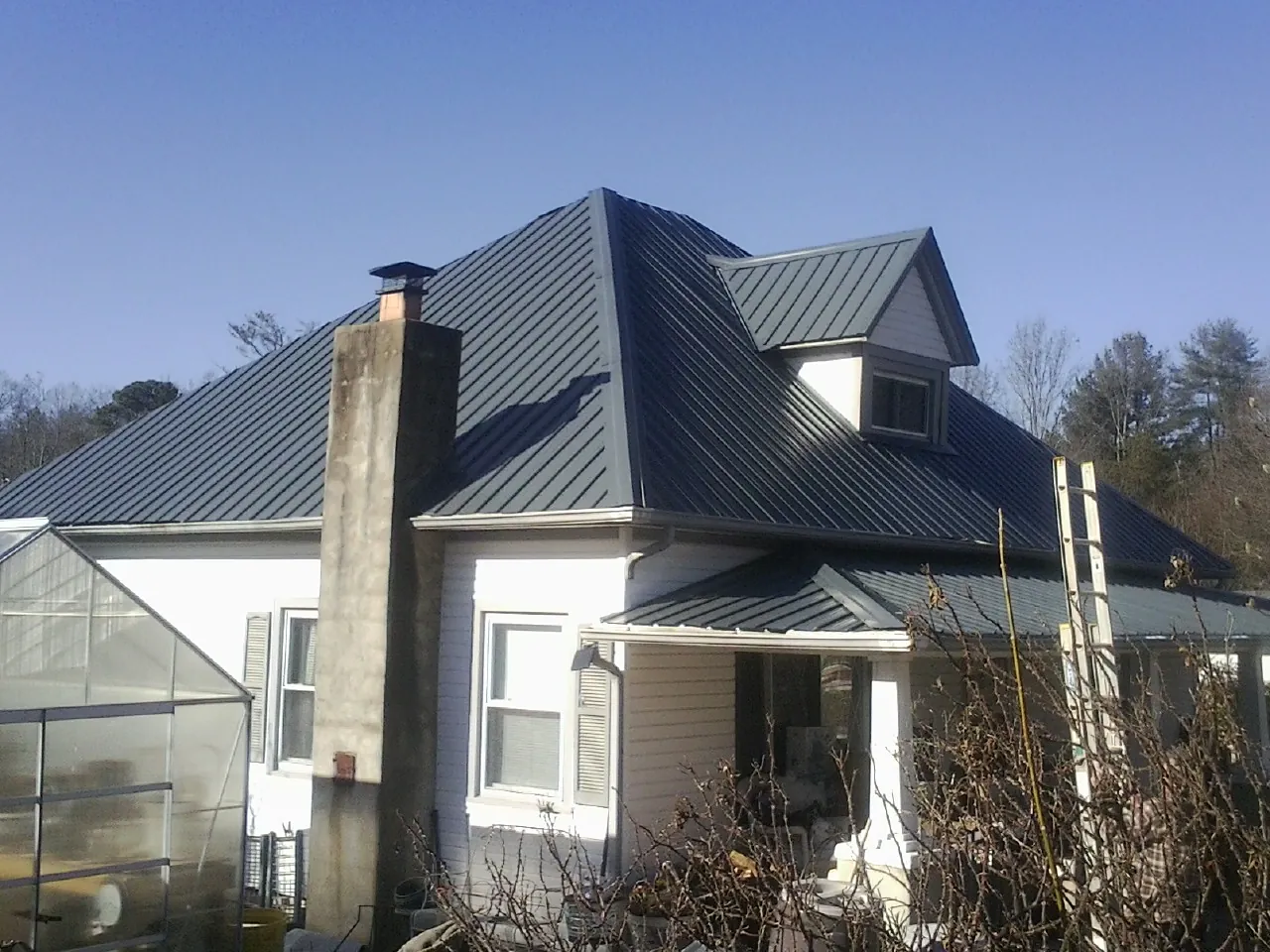 Dark blue standing seam metal roof on a white farmhouse with dormer — Slate & Tile Roof Repair by Roofing Brothers in Vanderbilt