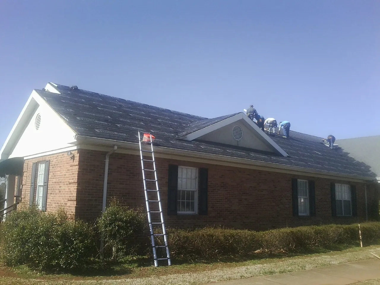 Crew tearing shingles off a brick ranch roof with a ladder set — Metal Roof Repair work by our crew in Vanderbilt