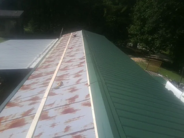 Old rusted panels beside newly installed green metal roofing — Wind Damage Roof Repair by Roofing Brothers in Vanderbilt
