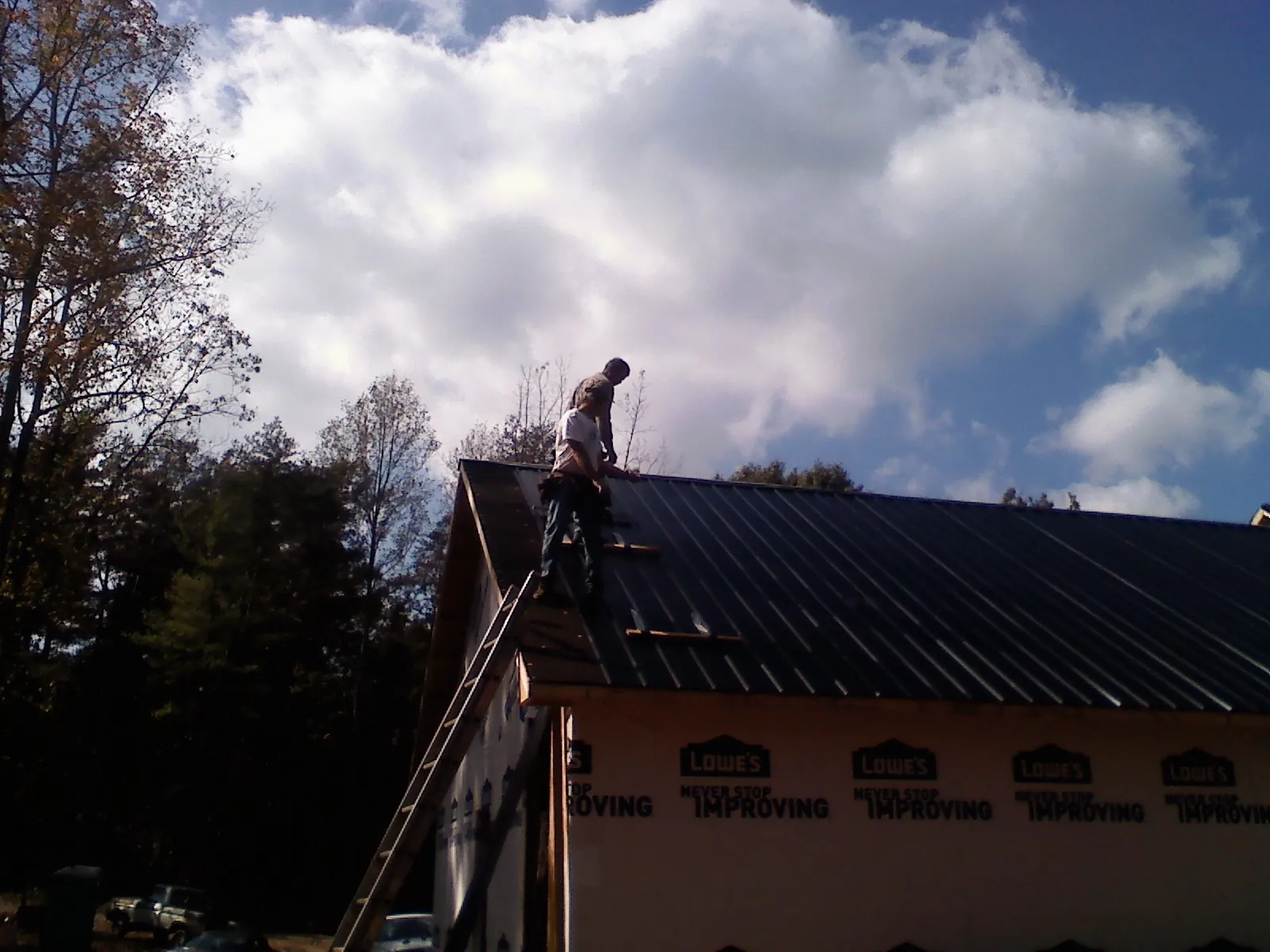 Roofer fastening dark metal panels high against a cloudy sky, from a Roof Inspection job in Vanderbilt
