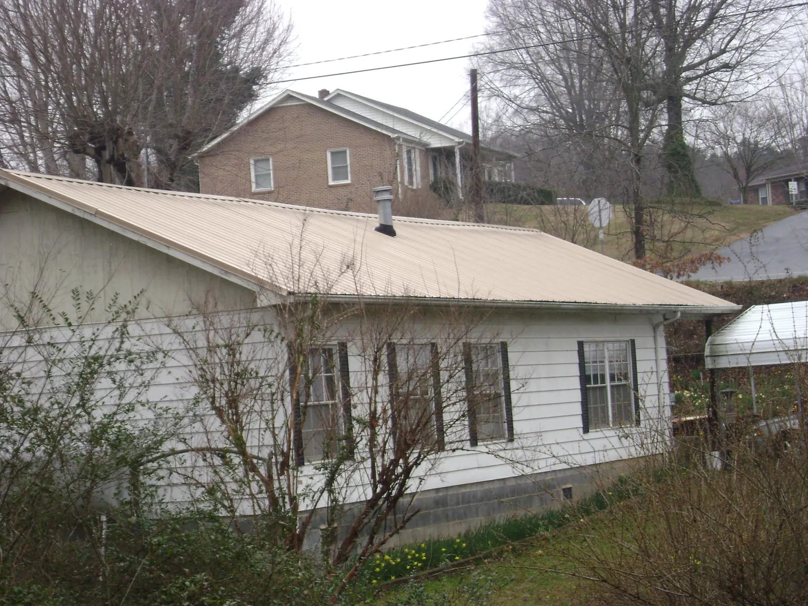 Tan metal roof on a white sided house set into a hillside — Commercial Roofing by Roofing Brothers in Vanderbilt